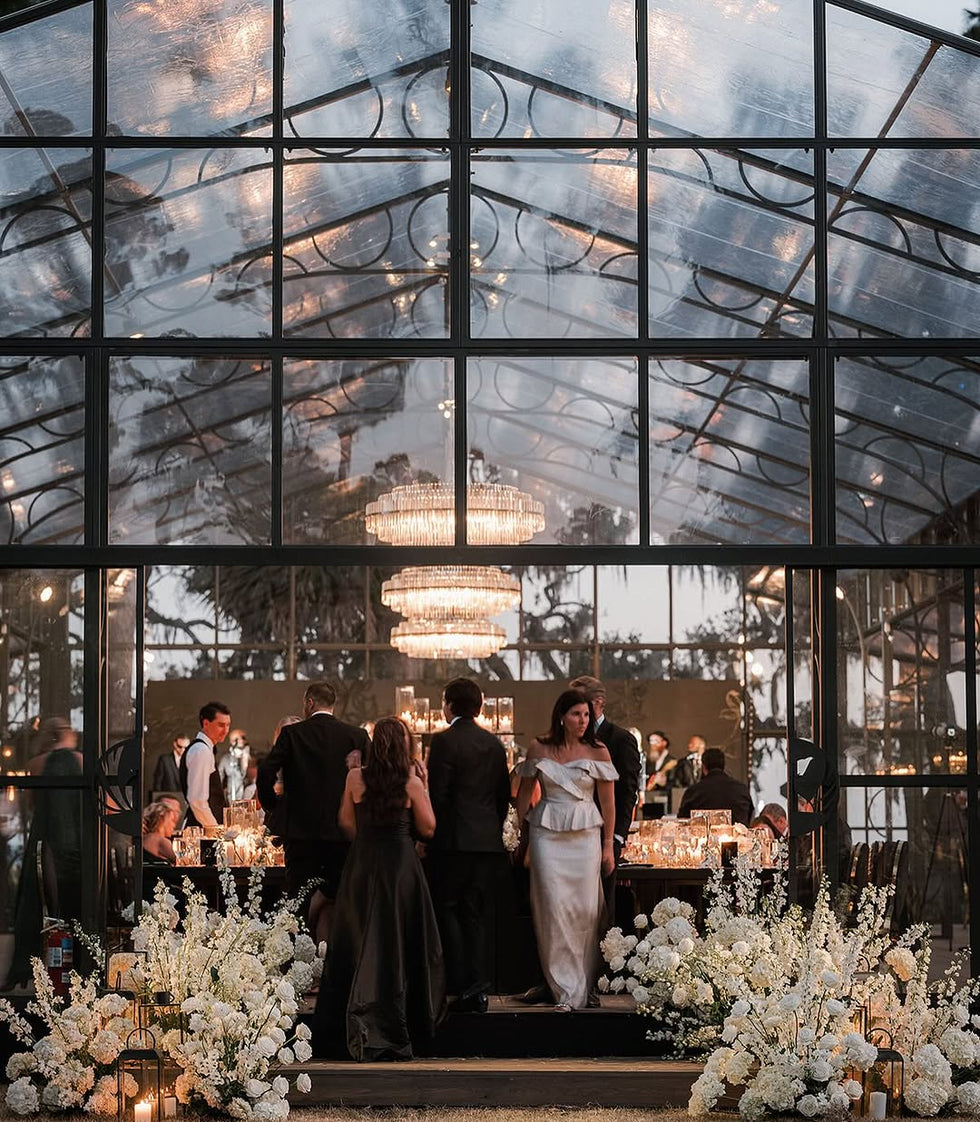 Chic black tie wedding reception by Meredith Tanton Events inside a glasshouse with dramatic chandeliers, white floral installations, and candlelit tables.